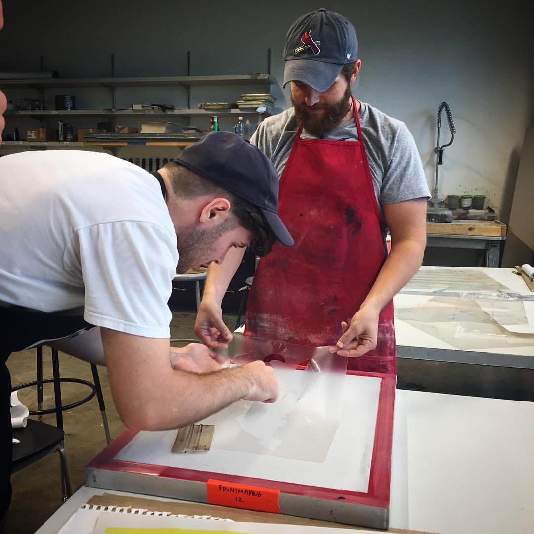 Work Study Student Terry Davis assists Associate Professor Justin Henry Miller in applying a hand cut stencil for screenprinting.