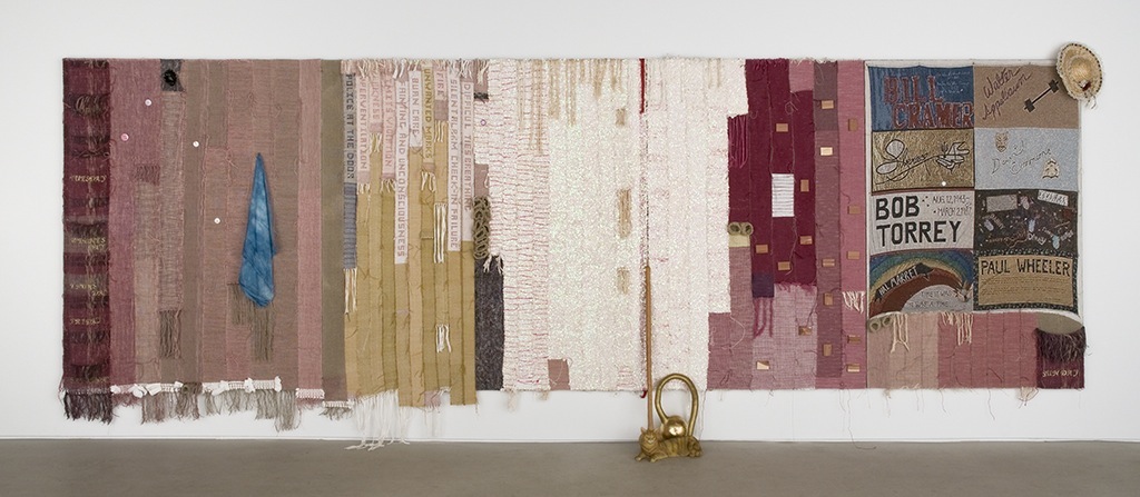 Josh Faught. It Takes a Lifetime to Get Exactly Where You Are, 2012; handwoven sequin trim, handwoven hemp, cedar blocks, cotton, polyester, wool, cochineal dye (from ground cochineal insects), straw hat with lace, toilet paper, paper towels, scrapbooking letters, Jacquard-woven reproduction of a panel from the AIDS Memorial Quilt, silk handkerchief, indigo dye, political pins, disaster blanket, gourd, gold leaf, plaster cat, cedar blocks, and nail polish; 8 x 20 ft. Courtesy of Lisa Cooley, New York.